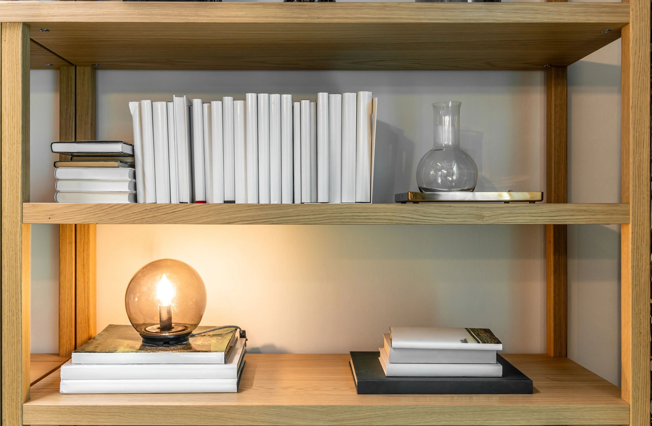 Minimal light-wood shelving with books and warm lamp glow